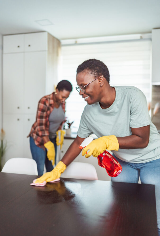 Two cheerful African women are cleaning the kitchen table and floor